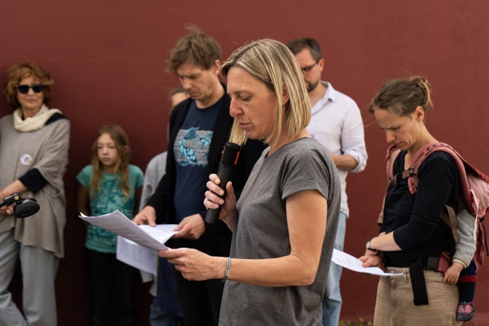 Frau redet am Mikrofon. Menschengruppe hört zu