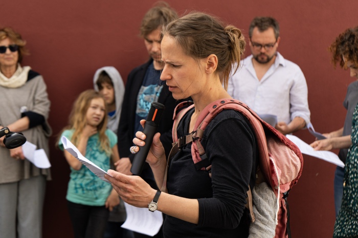 Frau redet am Mikrofon. Menschengruppe hört zu