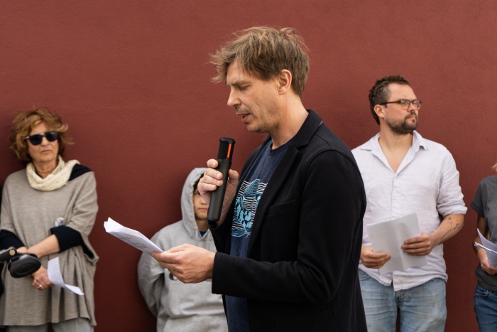 Mann redet am Mikrofon. Menschengruppe hört zu